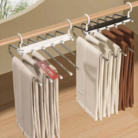 Two pants hangers holding trousers on a rail above a wooden floor